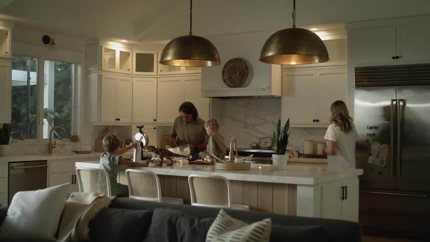 A woman walks into the kitchen and opens the fridge while the father prepares breakfast with the two boys