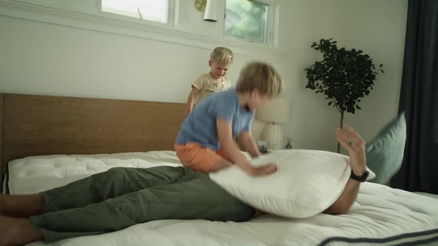 A father and his sons are pillow fighting on a mattress in the bedroom