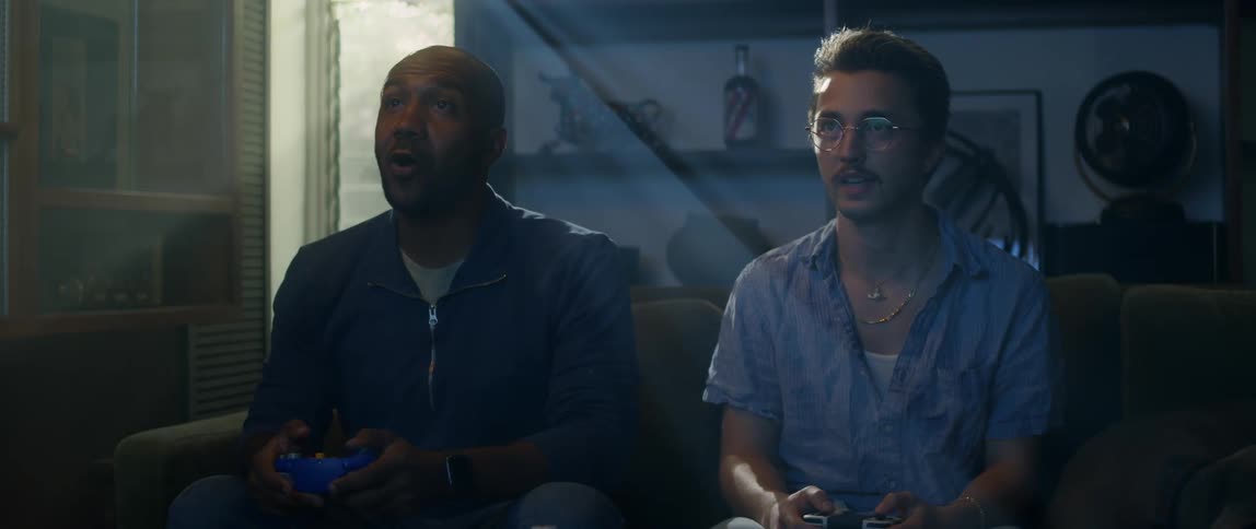 Two men sit on a couch at home and play a video game
