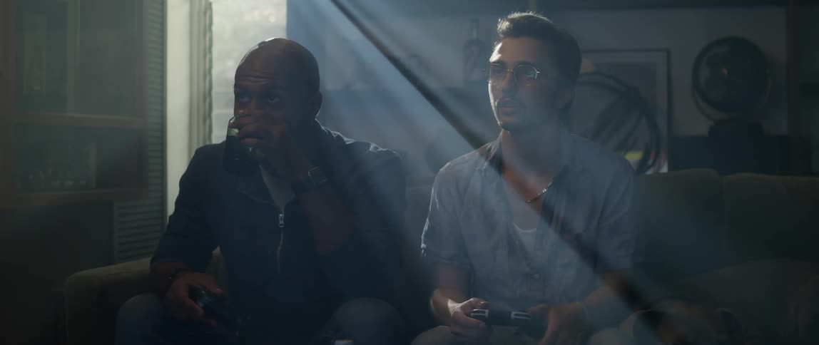 Male friends sitting on green couch and drinking from glasses play video game in the living room