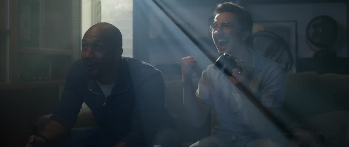 Two men laugh while playing video games on the couch