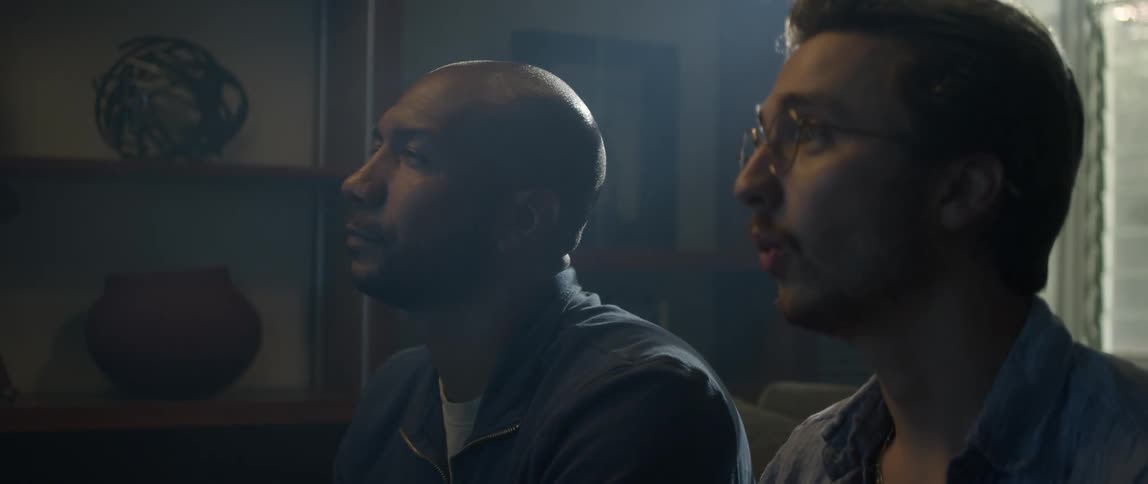 Two men sit on the couch watching something that ends up surprising one of them