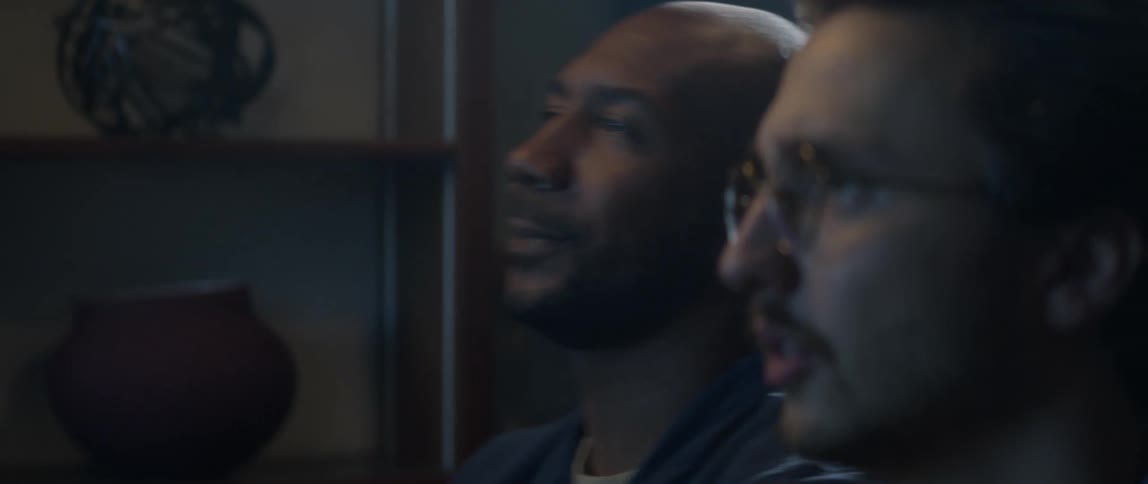 Two men sit on a couch watching something intently on tv