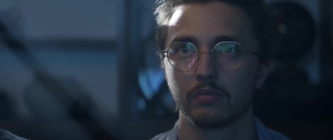 A man wearing wire frame glasses is making movements with his face and eyes