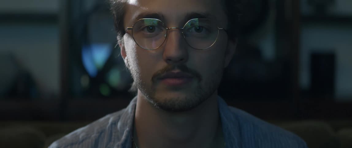 The camera shows a man by slowly moving from his chest to his face and the man smiles comically but is also somewhat off putting