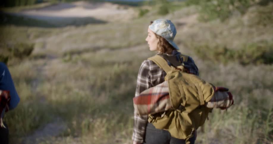 A man and woman walk through a field together towards the coast