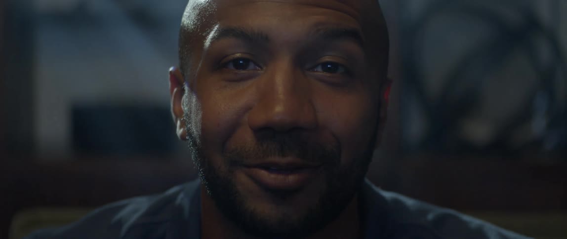 Man smiles and strokes his beard while talking as light from screen shines on his face