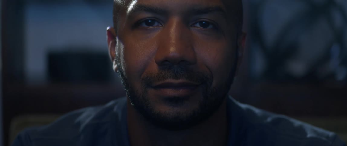 Man with blue jacket beard and shaved head looks at camera smiling