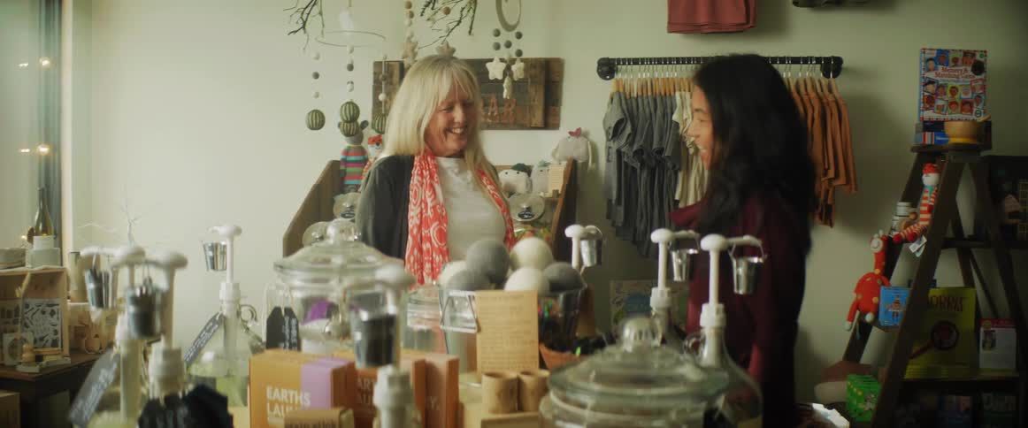 A woman is looking around in a small shop and a woman working in the store comes to help her