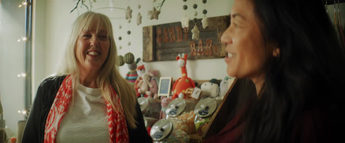 Middle aged women with fair and dark hair talk with each other in front of candy shelves in room