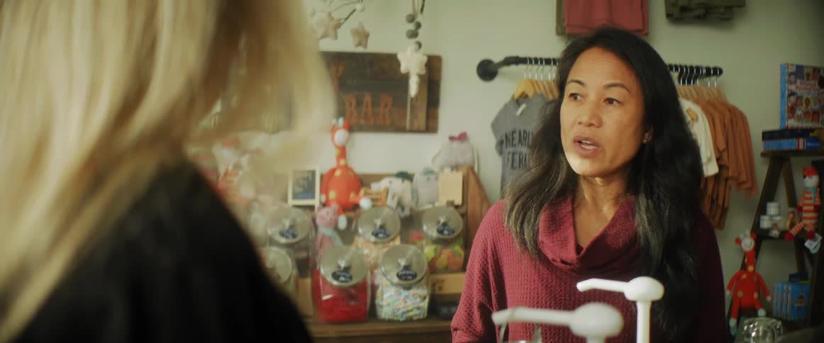 A shop owner speaks to a customer near products for sale