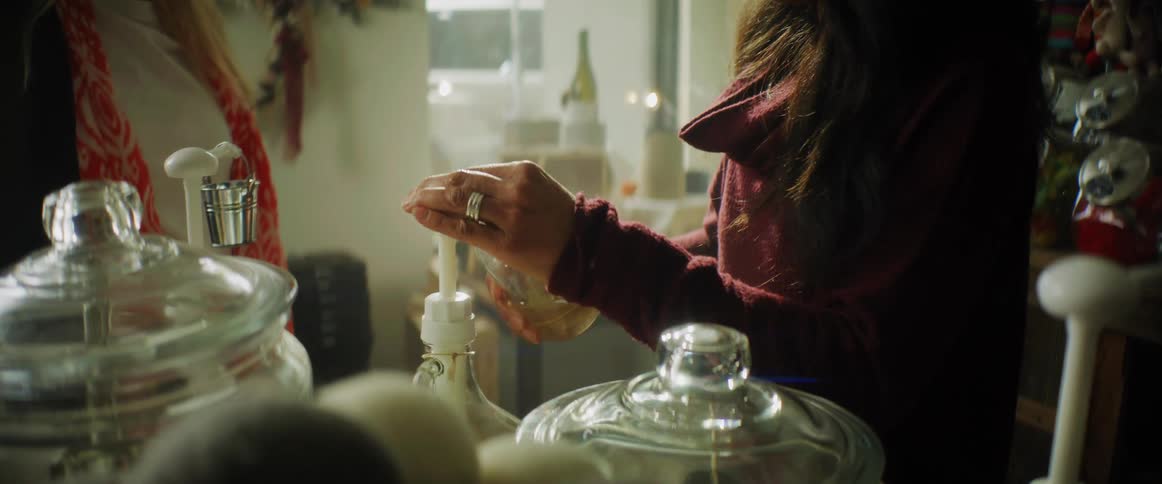 A woman is pumping a liquid into a glass jar for another woman while standing in a boutique