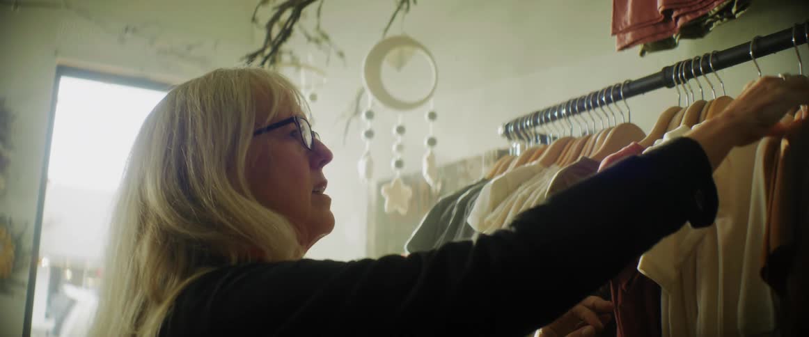 Middle aged woman wearing glasses and black sweater picks out clothes at clothes store