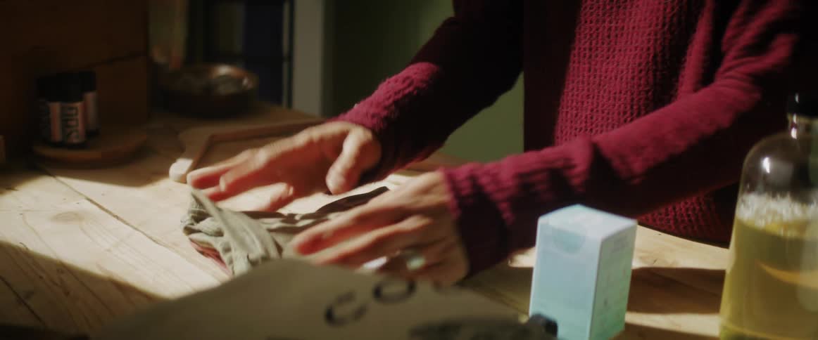 Person folds a tshirt on top of a table and then moves a jar of liquid