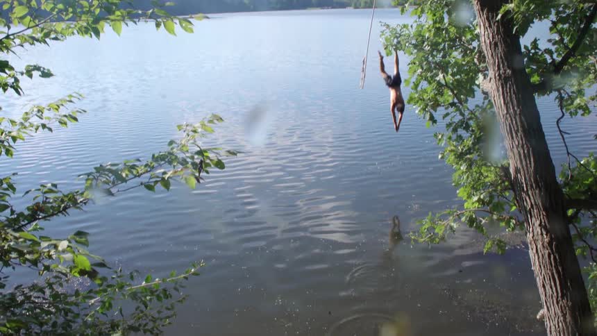 A man swings from a rope into a lake