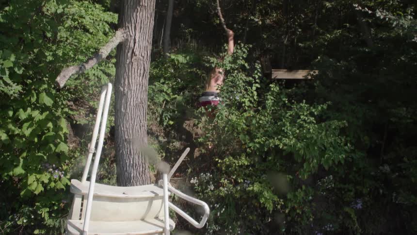 A man in swim trunks climbs a hill while holding a rope
