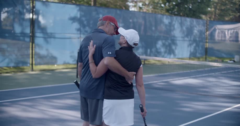 An older couple embrace on a tennis court
