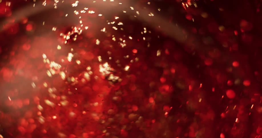 Light shines on gold particles as they swirl around in red liquid as it spins