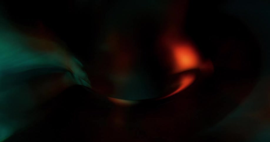 An arc of wobbling light changes colors as it quivers in the darkness