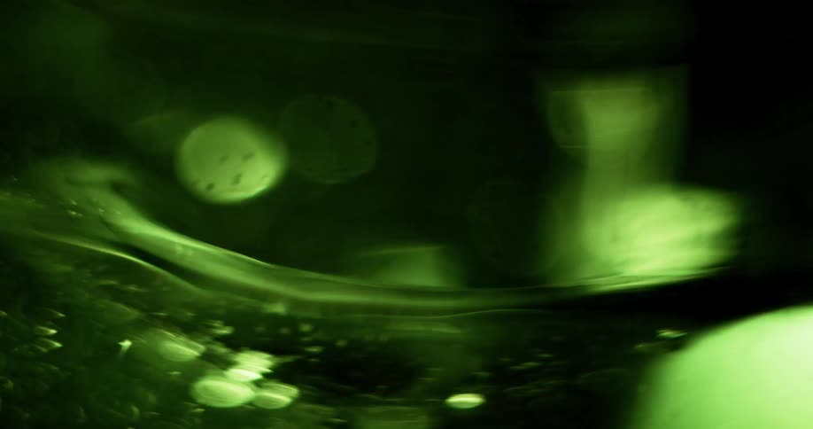 Close view of a whirlpool of water draining from a sink with green lighting in the background