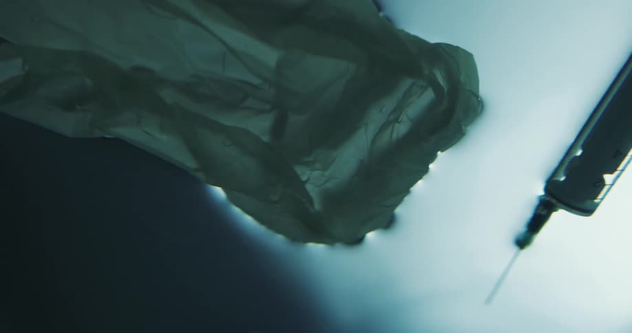 Syringe and needle and fabric float on surface of water showing signs of surface tension