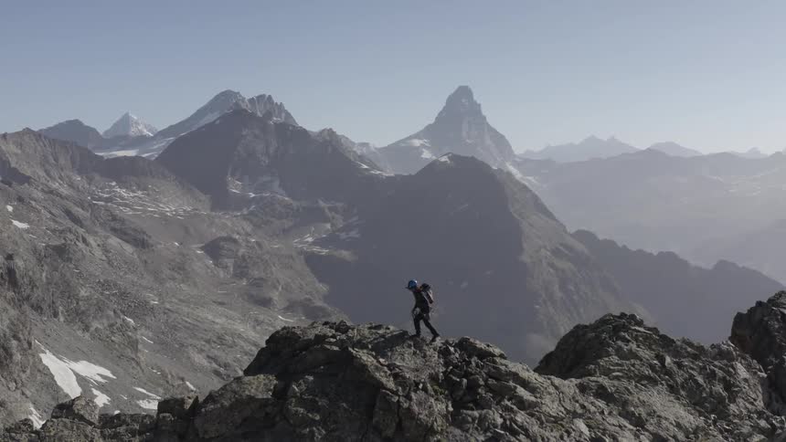 Mountaineer carrying rope moves across ridge overlooking valley filled with fog