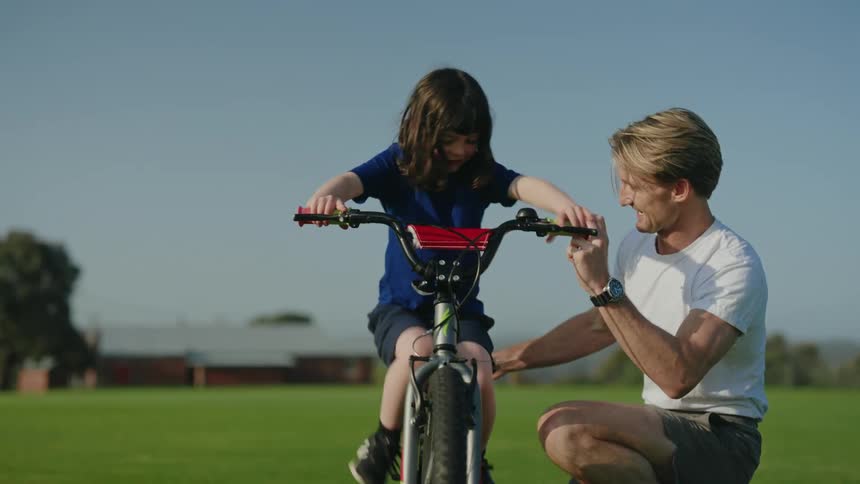 A man holds a bicycle upright as a child climbs onto it