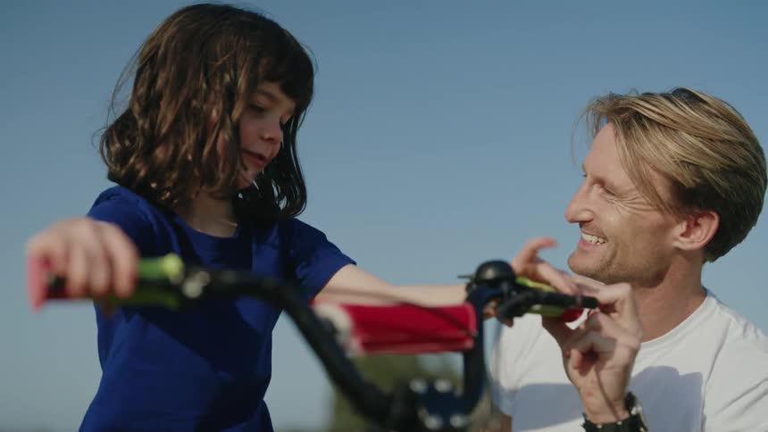 Father and daughter smile as he teaches her how to handle a bike