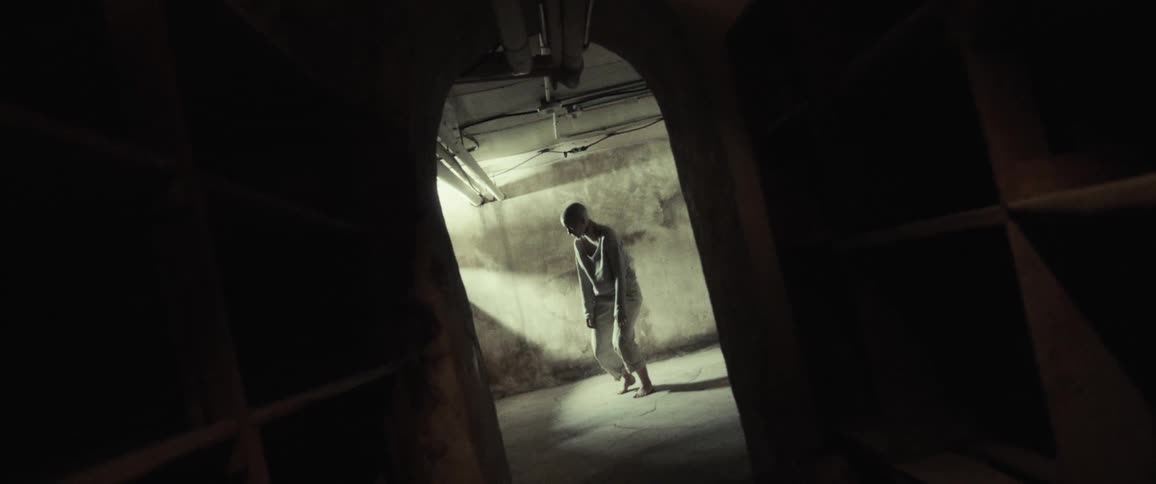 Woman in brightly lit room shown in doorway from dark room straightens