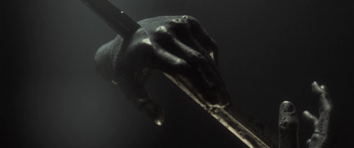 Sculpture of hands run through by sword rotate under light in a dark room
