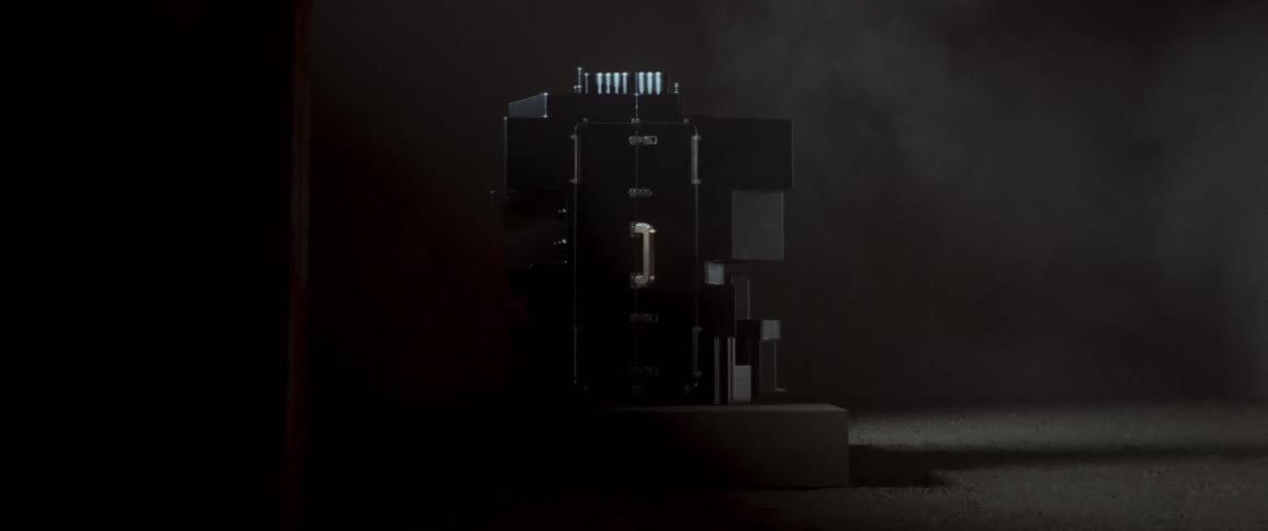 Sculpture sits on low platform on ground in dimly lit empty room