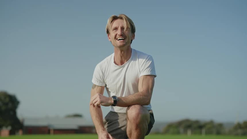 A man is in a field teaching his young daughter how to ride a bicycle and he gets down on one knee and laughs when she takes off