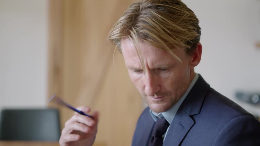 A man writes at a desk while referencing a graph on a laptop and a book