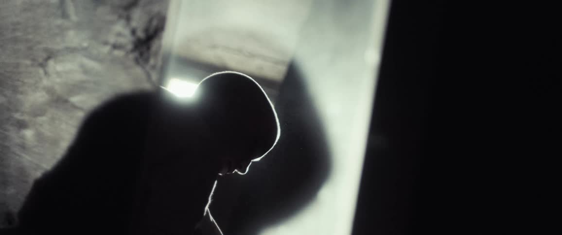Silhouetted woman crouches beside mirror and looks away