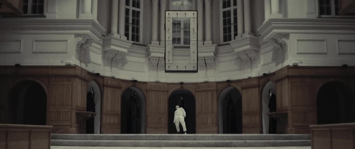 Woman below a floating sculpture with shadowy figures surrounding them
