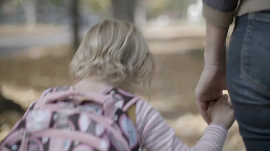 A little girl wearing a backpack walks hand in hand with an adult female