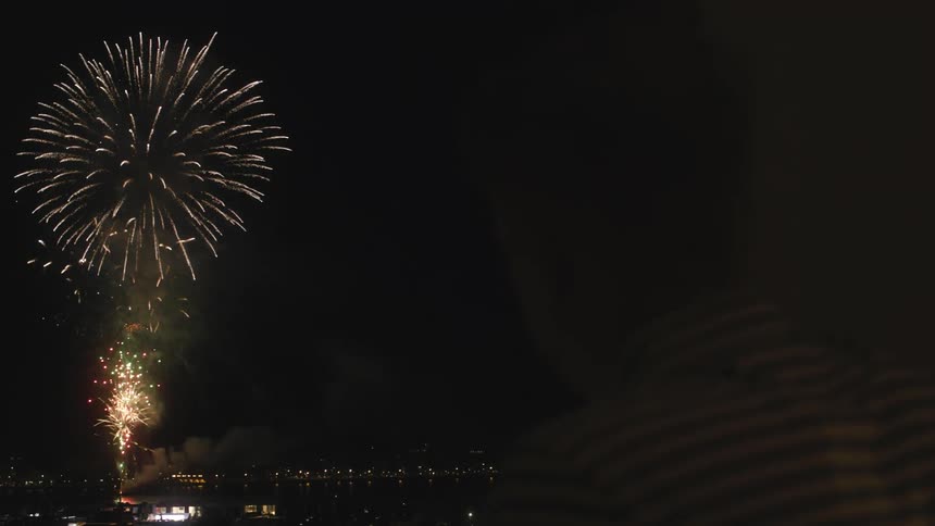 Fireworks explode over a waterfront in a city at night