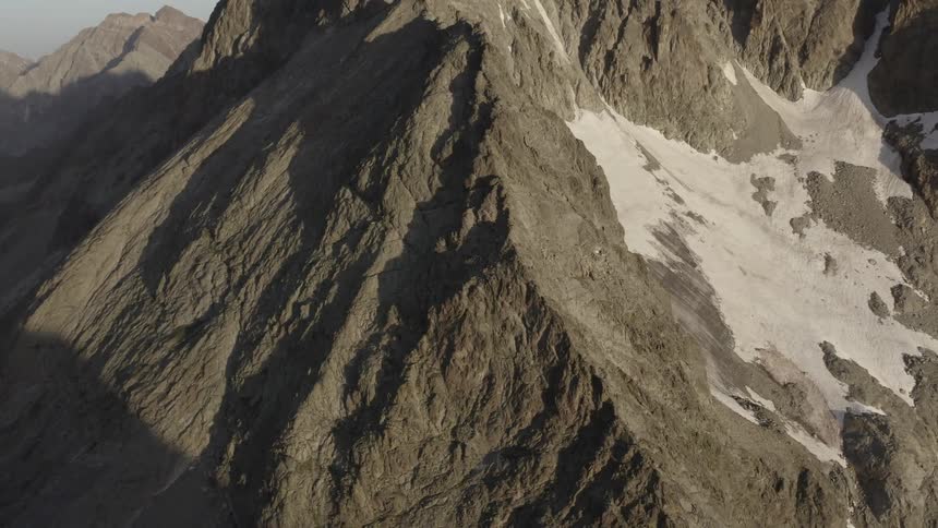 Snow covers portion of surface of mountain facing the sun while shadow fills crevices and the other sides of the mountain