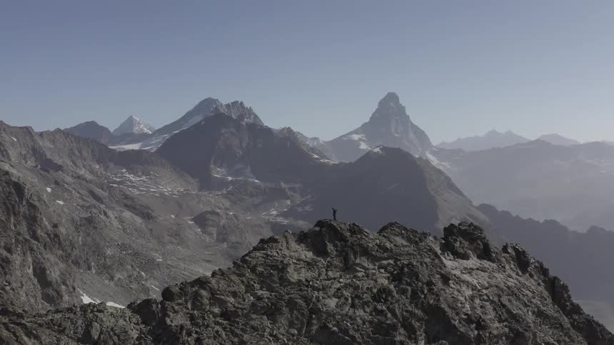 An aerial view of a person standing on a peak on a mountain range