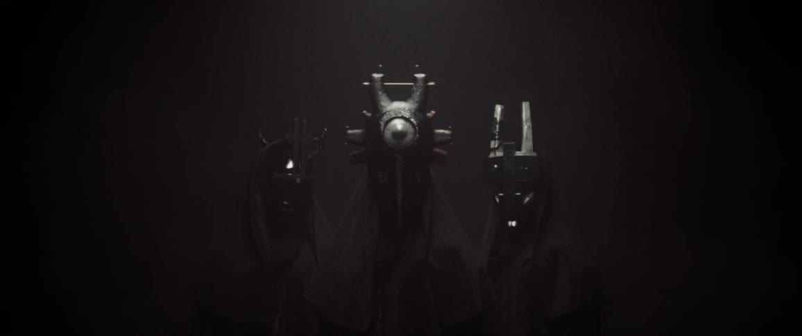 People wearing tribal masks and cloaks stand together in darkness