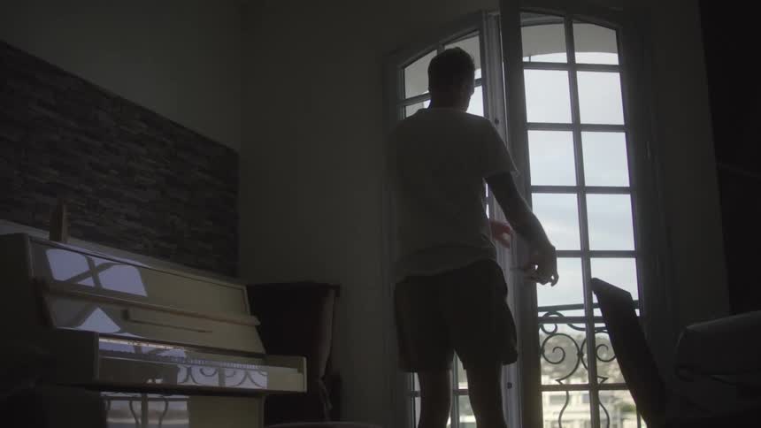 Man in white shirt and boxer opens the balcony door next to upright piano in room