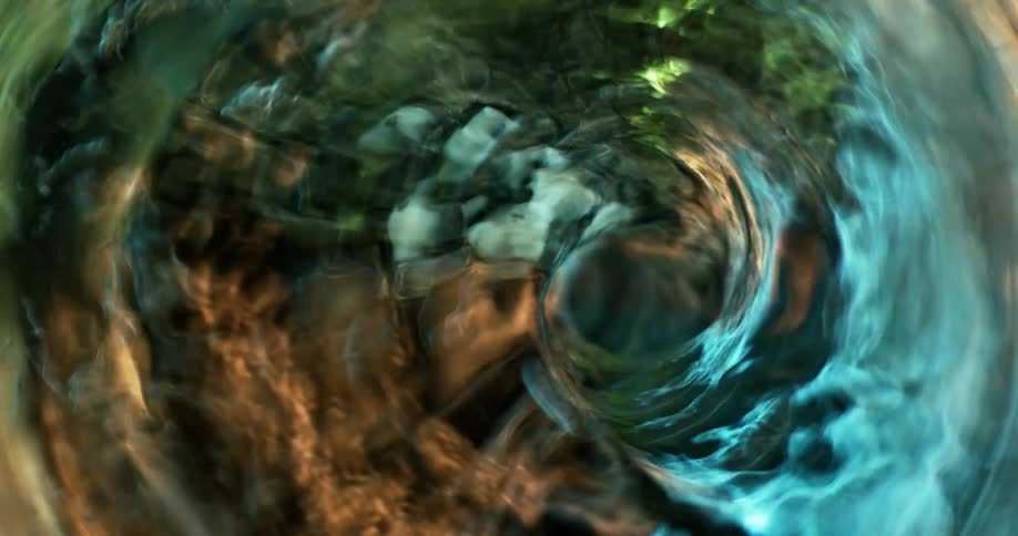 Liquid flows down the tunnel of a swirling vortex as blue and orange light reflects on the surface