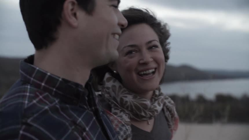 A man and a woman walk while talking and laughing on an overcast day