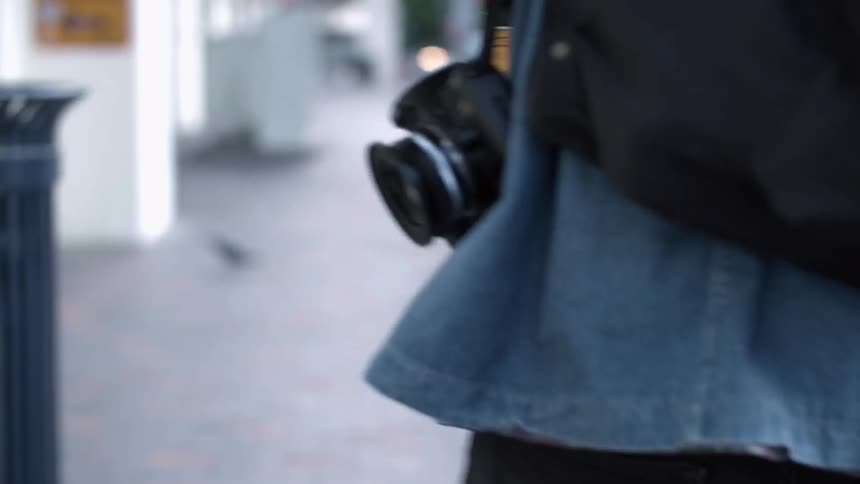 A person carries a camera while walking in a city during the day