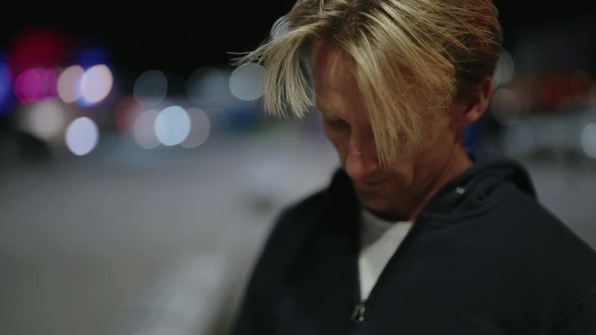 Man standing outdoors at night puts earbuds into his ears