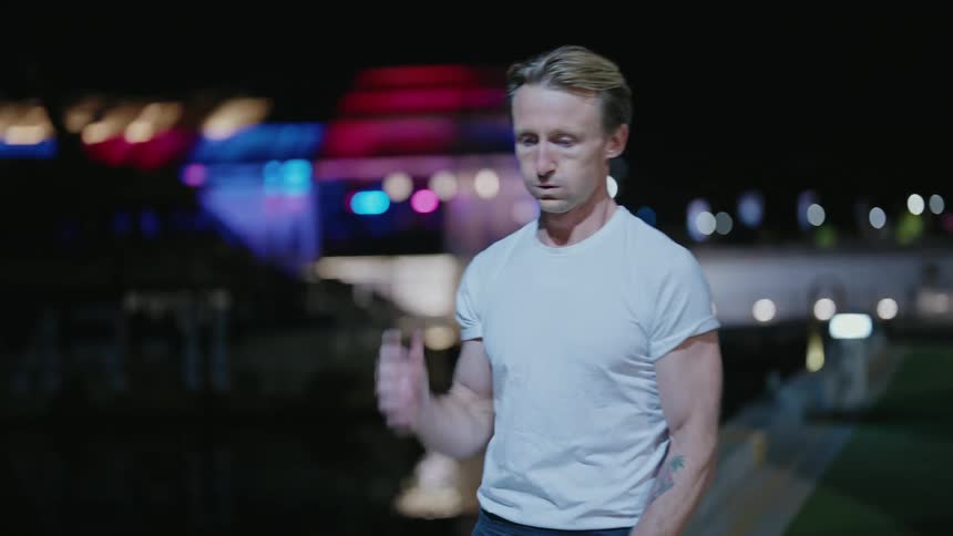 A man next to a river breathes heavy as he puts his earbuds back in during a run