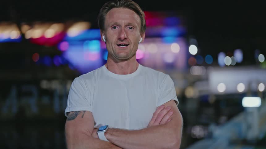 Man standing near water at night breathes deeply and smiles