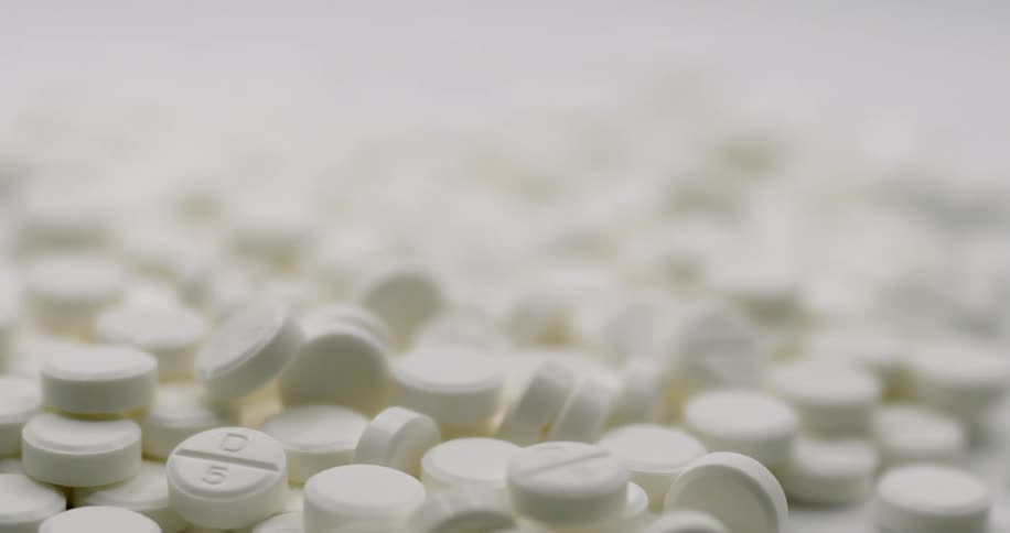 A pile of white pills are spread across a table