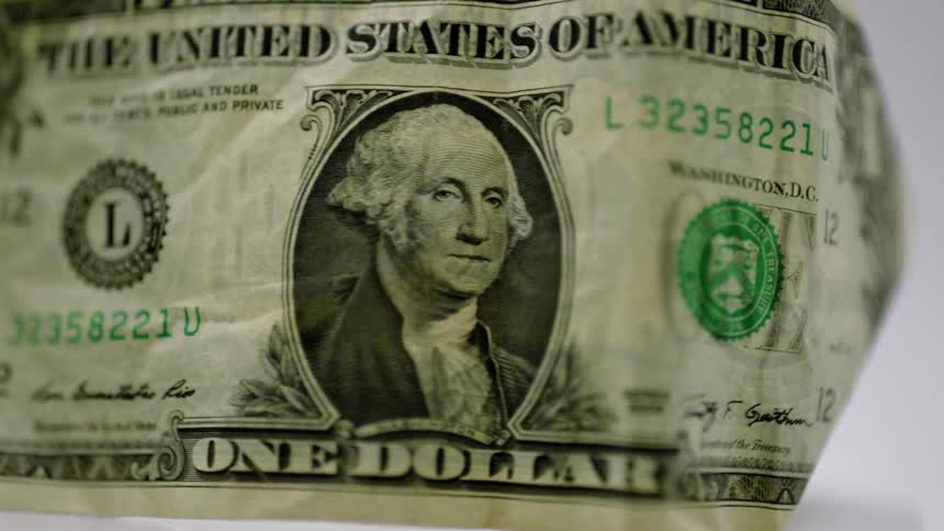 Slightly crumpled dollar bill rotates against a pale blue background