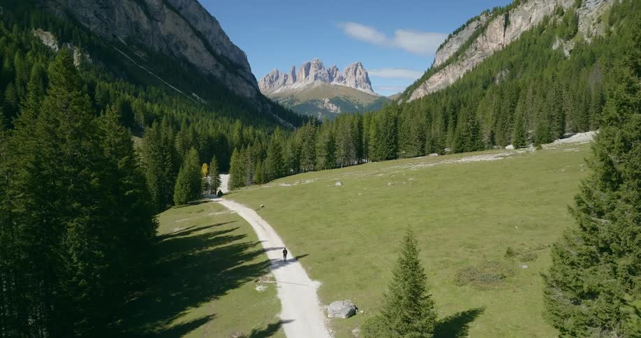 A person walking on a valley trail between mountain slopes on a bright day